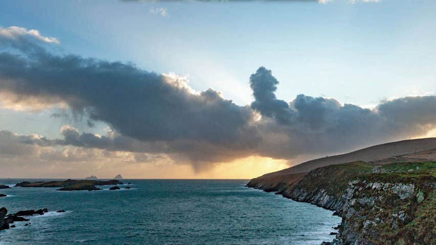The Skellig Islands visible in the distance against a cloudy sunset taken from an inlet on the Skellig Ring coast