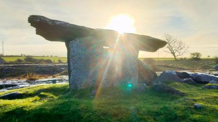View of a sunrise behind a portal dolmen with Anam Croí Ireland Tours