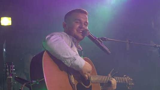 Singer, songwriter Dan McCabe playing a guitar and singing into mic on a stand.