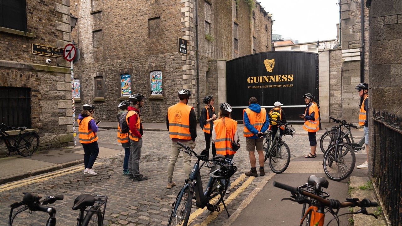 Group of people in orange high visibility vests on a cycling tour in front of the Guinness storehouse