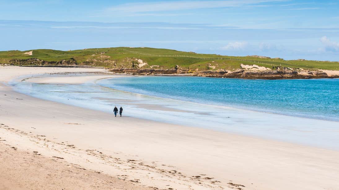Two people walking along the golden strand of Dog's Bay Beach in County Galway