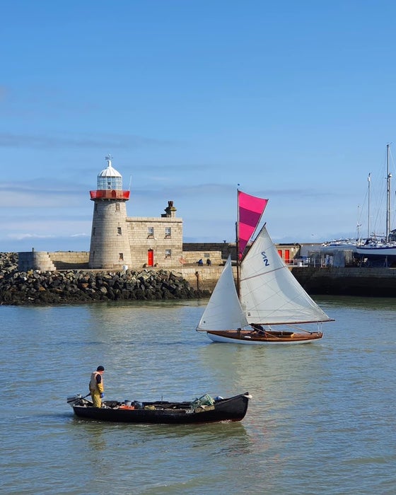Sailboat and fishing boat passing the lighthouse in Howth Harbour.