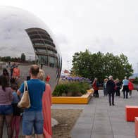 People looking at a large metal sphere in a city street