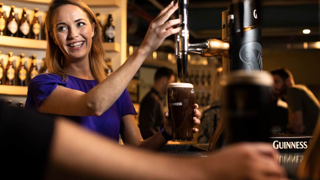 A woman smiling and pulling a pint at the Guinness Storehouse, Dublin