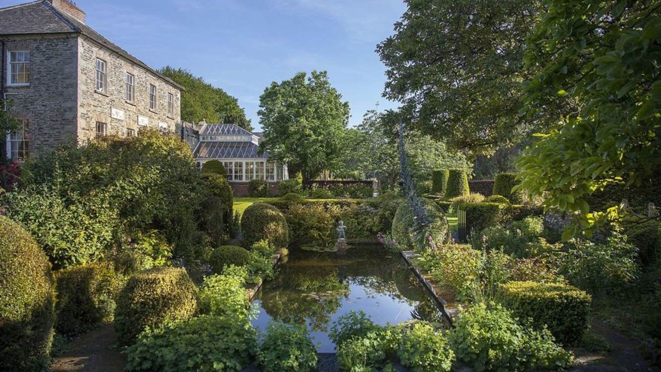 A large country house with a garden pond framed with shrubs and plants