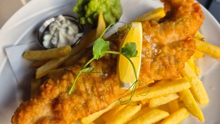 A plate of fish and chips served with tartar sauce and mushed peas
