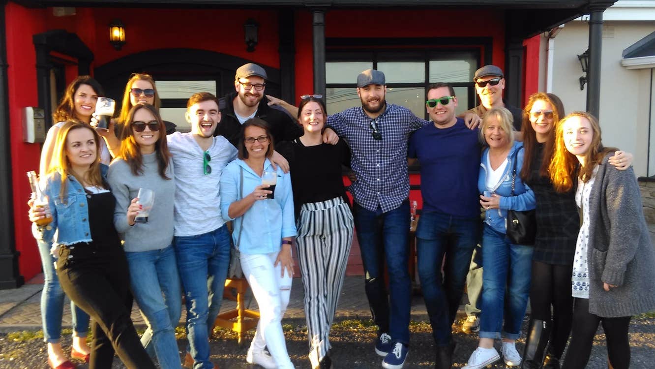 Group posing in front of a red and black building some holding drinks