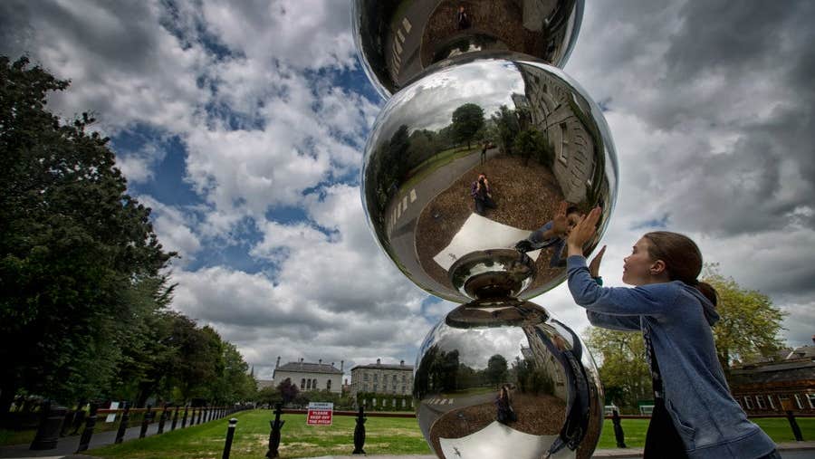 A girl looks at her reflection in the Atoms & Apples sculpture at Trinity College