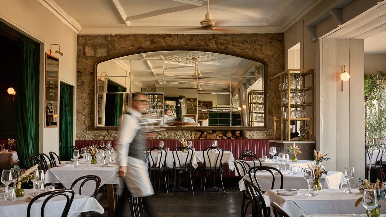 A member of staff walking through a dining room with a large mirror on the back wall