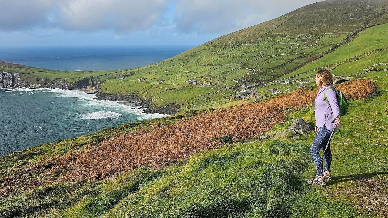 Person holding a walking pole standing in a field overlooking the sea