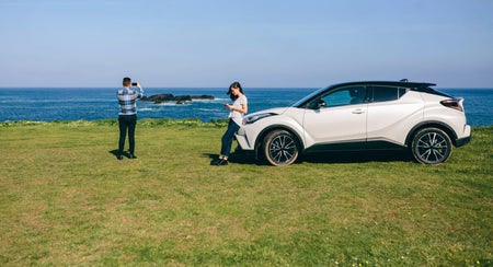 Two people at a coastal location beside a car