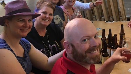 Six people holding glasses sitting at a wooden table with beer bottles on it