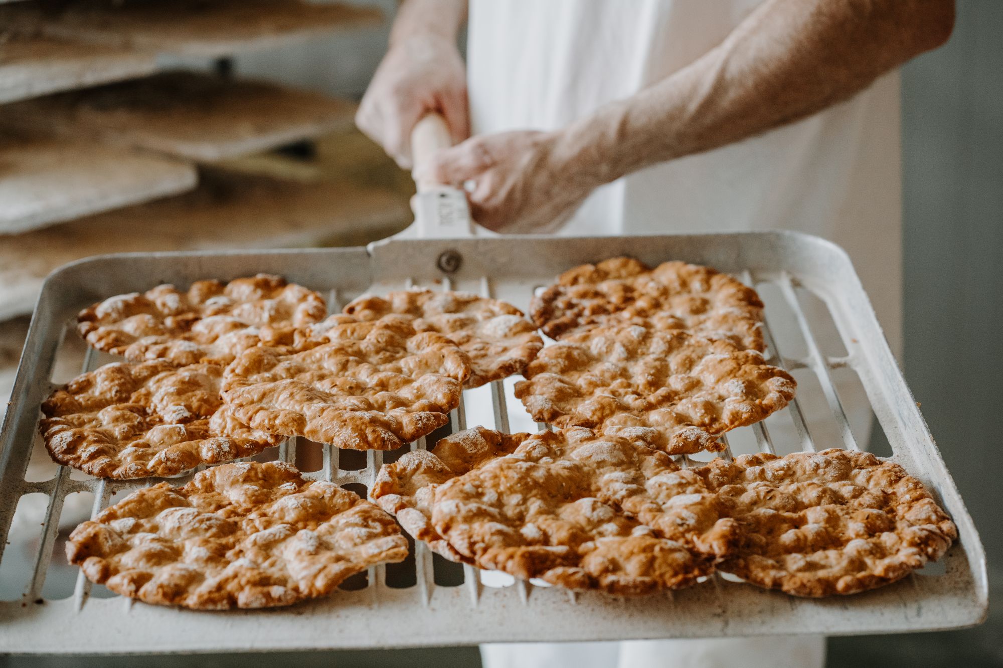 Bäcker nimmt ein Blech mit frisch gebackenem, goldbraunem Schüttelbrot aus dem Ofen.