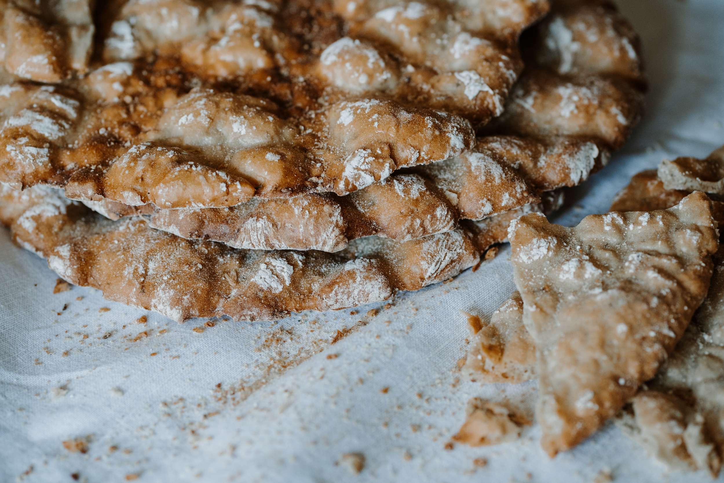 Schüttelbrot croccante spolverato di farina, con alcune fette spezzate su un telo chiaro.