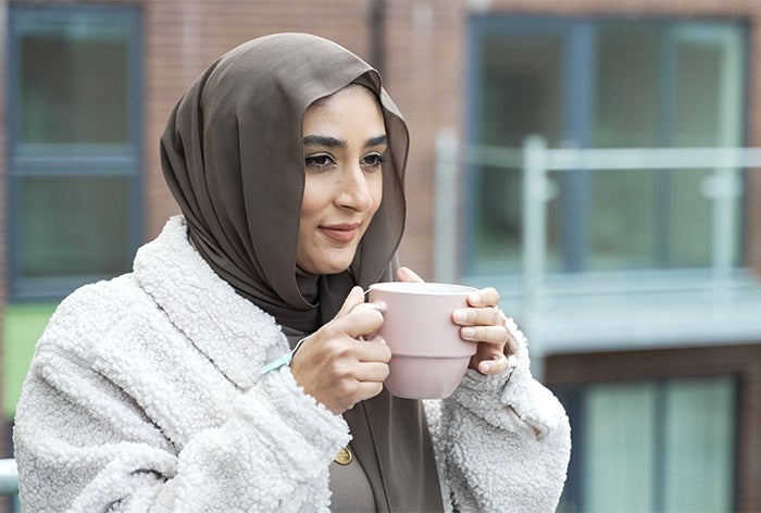 A lady standing on a balcony drinking a cup of coffee