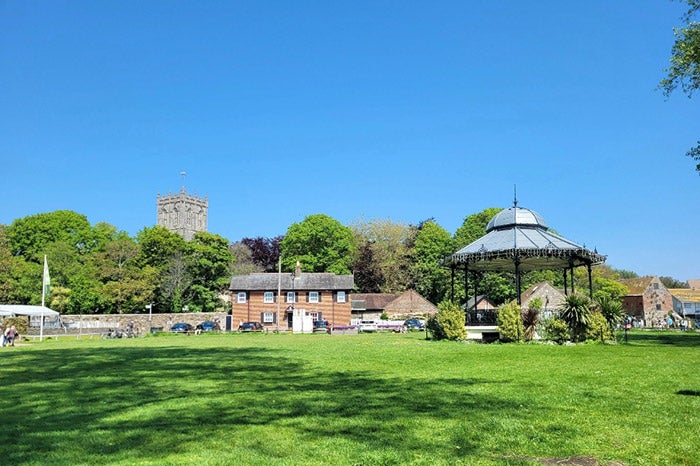 Grass and bandstand in the foreground, cloudless blue sky and priory in the background 