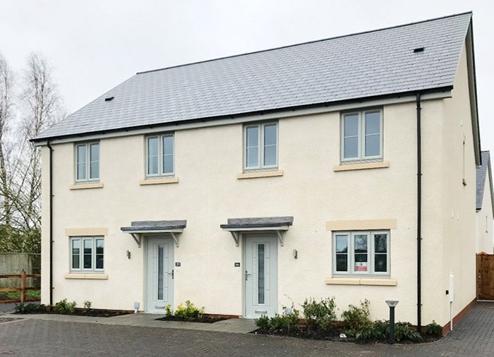 Two semi-detached houses with cream walls, grey roofs and pale green doors