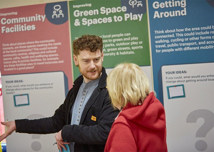 A man and a woman talking at a community event in front of some banners