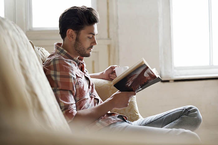 A man reading a book, sat down on a sofa.